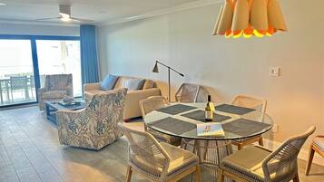 A modern living room with a round glass table, wicker chairs, a sofa, and a ceiling fan.