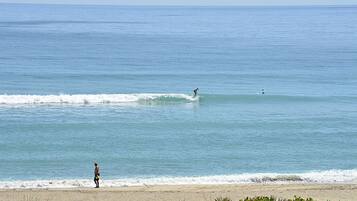 Une plage aux vagues douces, un surfeur et une personne debout sur le rivage.