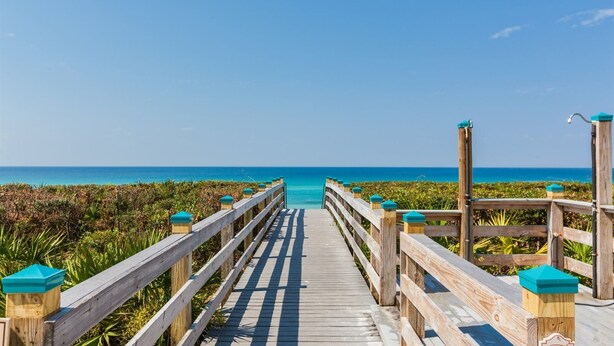 Une promenade en bois qui mène à une plage d’où l’on a une vue dégagée sur l’océan.