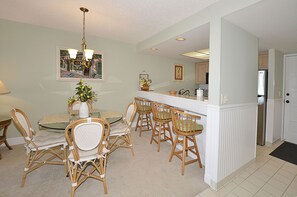 A dining area with wicker chairs, a glass table, and a chandelier.