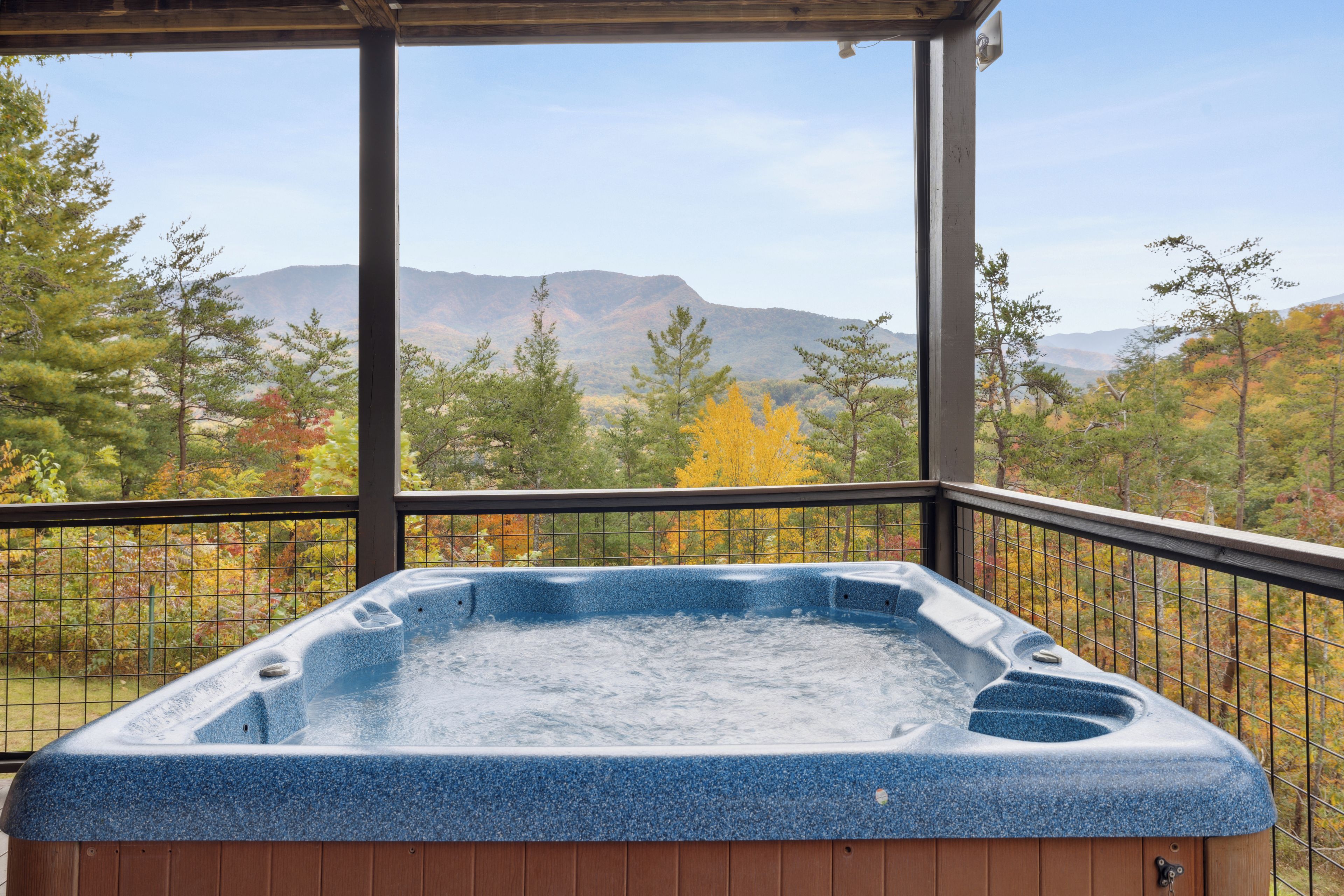 Un bain à remous situé dans un espace extérieur abrité, offrant une vue sur les montagnes et les arbres aux couleurs automnales.