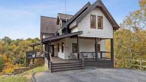 A two-story house with a porch, a staircase leading to the upper level, and a view of the surrounding forest.