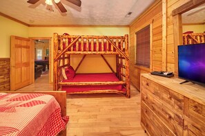 A bunk bed with a red mattress, a wooden dresser with a television, and a wooden ceiling fan.