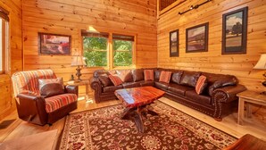 A cozy cabin interior with a leather sofa, a patterned armchair, a wooden coffee table, and a large rug.