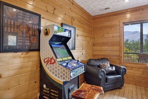 A wooden cabin interior with a gaming console, a leather armchair, and framed artwork on the wall.