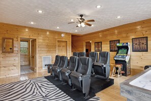 A log cabin interior with a ceiling fan, a row of reclining chairs, a gaming machine, and a hot tub. - Cabin w/Amazing Mountain Views-Theater-Game Room (GATLINBURG)