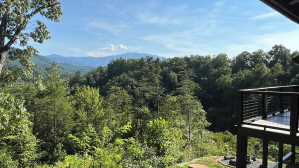 A view from a wooden deck overlooking a forested valley with mountains in the distance.