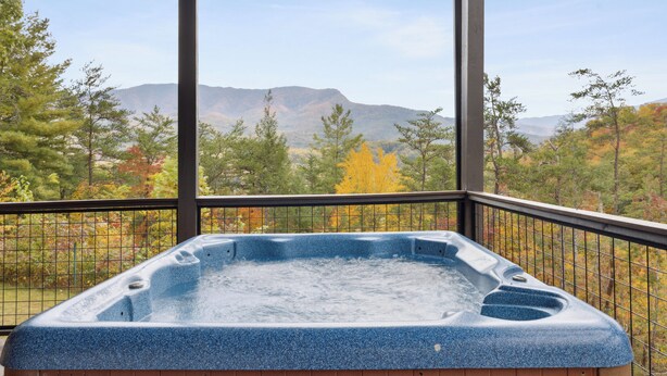 A hot tub in a covered outdoor area with a view of mountains and autumn trees.