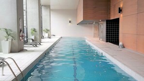 Ein Schwimmbecken mit gefliestem Sonnendeck, Liegestühlen und Topfpflanzen.