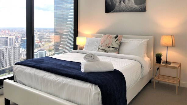 Ein modernes Hotelzimmer mit einem großen Bett, zwei Nachttischlampen, Blick auf die Stadt und einem abstrakten Kunstwerk an der Wand.