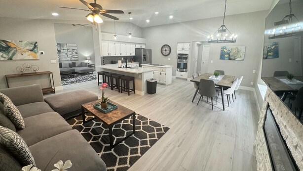 Un espace de vie et de salle à manger moderne à aire ouverte, comprenant une cuisine, un ventilateur de plafond et une table à manger avec des chaises.