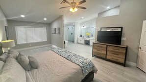 Une chambre moderne avec un grand lit, un ventilateur de plafond, une télévision et un dressing.