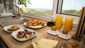 A breakfast setting with plates of toast, jam, cheese, and croissants, along with two glasses of orange juice and a bottle of olive oil. - Olea Escape - Your own house in an exclusive olive estate | Stunning 360° Views (Githio)