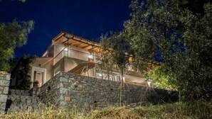 A stone-walled building with a balcony, surrounded by trees and vegetation. - Olea Escape - Your own house in an exclusive olive estate | Stunning 360° Views (Githio)