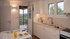 A compact kitchen with white cabinets, a built-in oven, and a small dining area with a table set for two. - Olea Escape - Your own house in an exclusive olive estate | Stunning 360° Views (Githio)