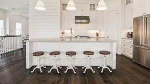 A modern kitchen with white cabinetry, a central island with stools, stainless steel appliances, and pendant lighting.