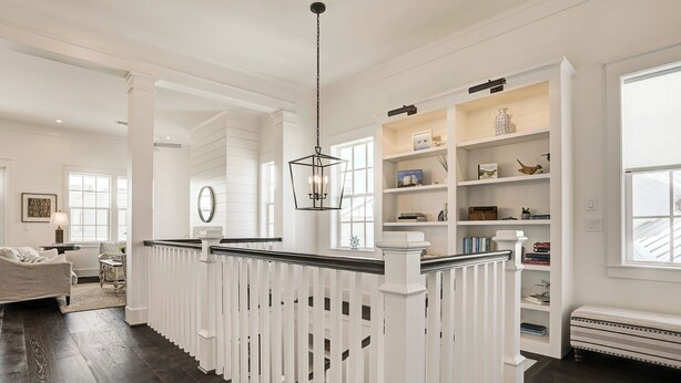 A spacious living area with a white railing, a fireplace, and a bookshelf.