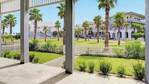 A covered outdoor area with a view of a building complex, palm trees, and a white picket fence.