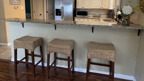 A kitchen with a central island, white cabinets, a stainless steel refrigerator, and a microwave. There are three woven stools at the island. - Waterfront Home! Relax & Enjoy the Serenity of Lake Palestine.  
 (Chandler)