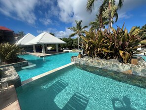 A clear blue pool with a stone border, a covered pavilion, and tropical plants. - Corner Suite "Glass House on the Sea" Modern Luxury on Sapphire Beach (St. Thomas)