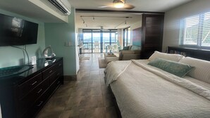 Un dormitorio con cama, televisor, ventilador de techo y vista al exterior.