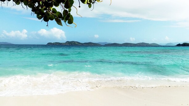 Una playa con agua turquesa cristalina y islas a lo lejos.