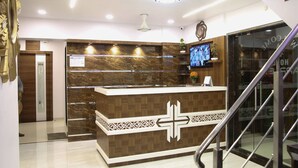 A reception area with a marble counter, a cross design, a clock, and a television. - Hotel Apple Inn (Navi Mumbai)