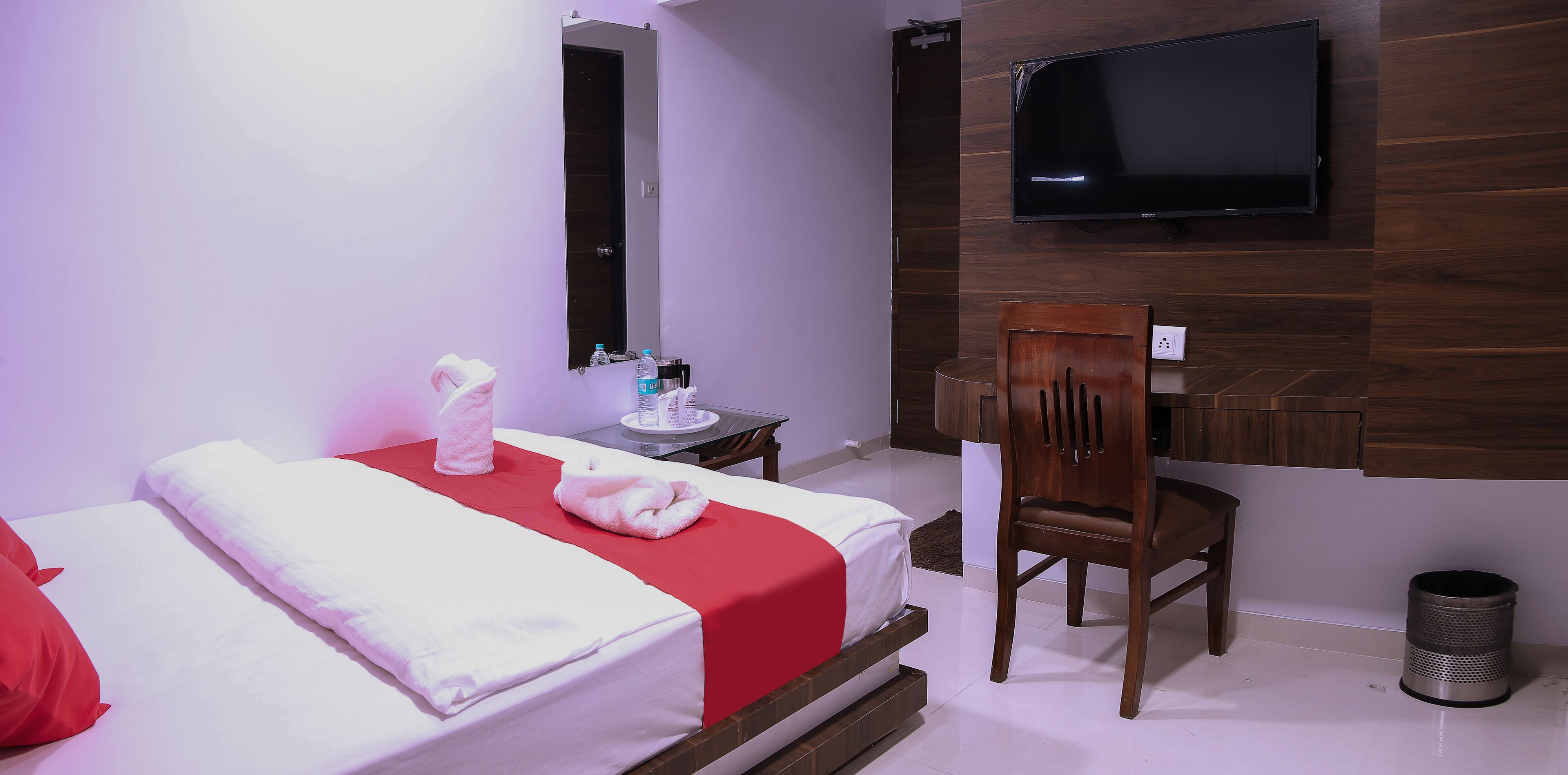 A hotel room with a bed, a desk, a chair, a TV, and a trash can.
