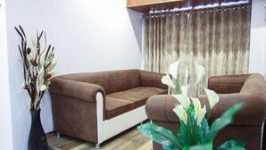 A modern living room with a brown leather sofa, a black vase with dried flowers, and a green plant. - Hotel Apple Inn (Navi Mumbai)