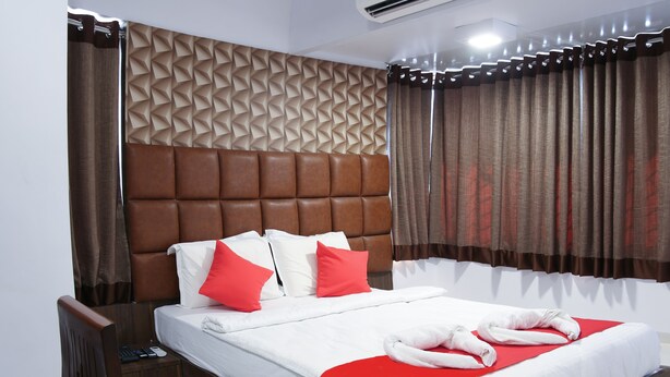 A hotel room with a large bed, a headboard, a red accent pillow, a white bedspread, and a red accent pillow. - Hotel Apple Inn (Navi Mumbai)