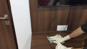 A person cleaning a wooden TV stand with a cloth and gloves. - Hotel Apple Inn (Navi Mumbai)