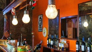 A bar area with hanging light bulbs, a variety of bottles, and a rustic stone wall. - Cabaña - Bar- Restaurante El Mirador (Vallegrande)