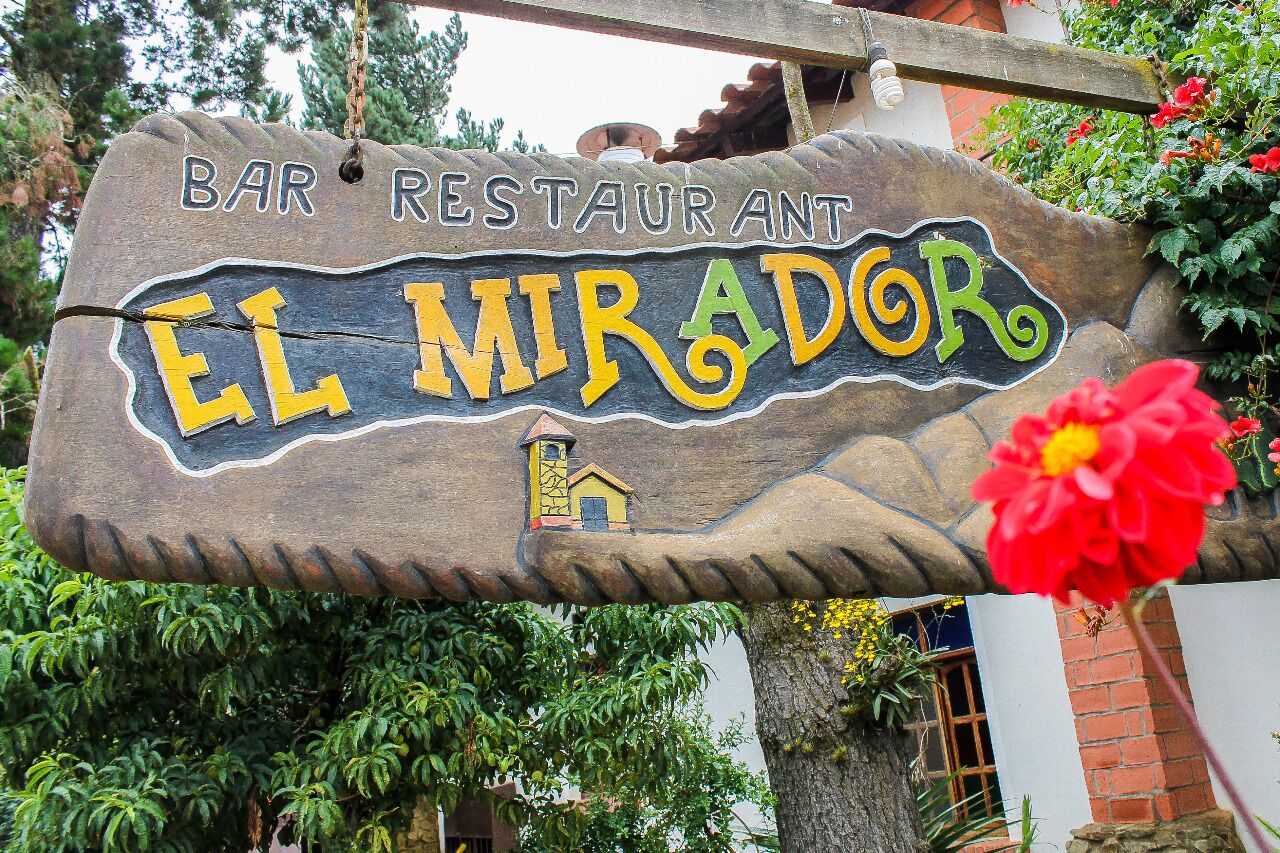 A wooden sign for 'BAR RESTAURANT EL MIRADOR' with a small house illustration.