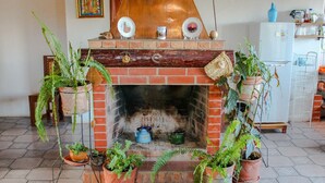 A rustic fireplace with potted plants, a brick wall, and a white refrigerator in the background. - Cabaña - Bar- Restaurante El Mirador (Vallegrande)
