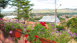 A balcony with red and purple flowers, a view of a town with buildings and hills in the background. - Cabaña - Bar- Restaurante El Mirador (Vallegrande)