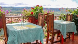 Two tables with checkered tablecloths, wooden chairs, and a view of mountains in the background. - Cabaña - Bar- Restaurante El Mirador (Vallegrande)