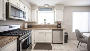 Een moderne keuken met witte kastjes, een roestvrijstalen fornuis, een magnetron en een koffiezetapparaat.