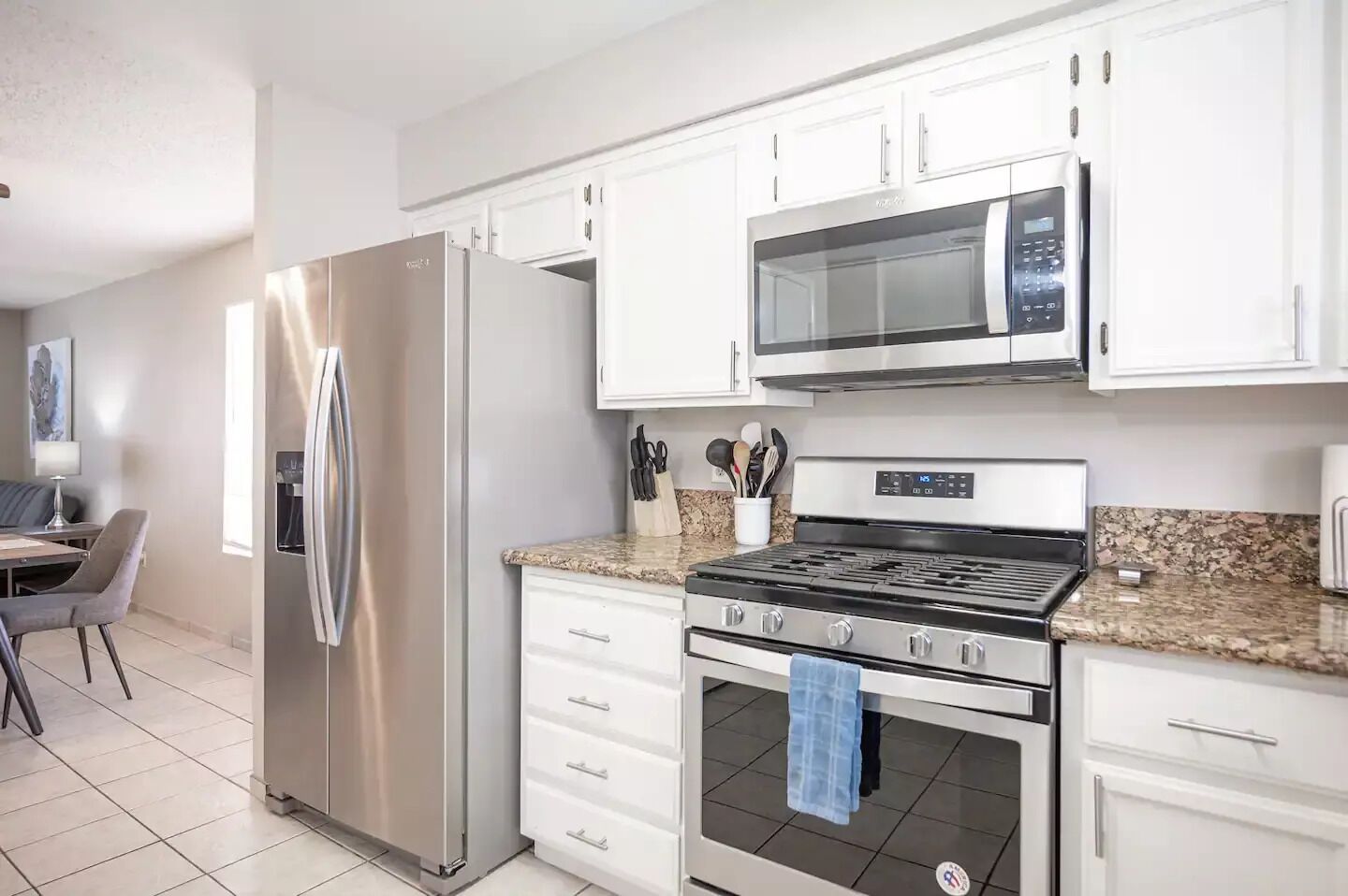 A modern kitchen with white cabinets, stainless steel appliances, a granite countertop, and a dining area with a table and chairs.
