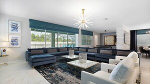 A modern living room with a sectional sofa, a coffee table, and a chandelier. - VIP Home Near Disney w Toy BR, Huge Theater, Arcade, Ping Pong Table & Spa Pool (Kissimmee)