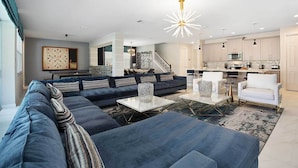 A modern living room with a sectional sofa, a coffee table, and a dining area with chairs. - VIP Home Near Disney w Toy BR, Huge Theater, Arcade, Ping Pong Table & Spa Pool (Kissimmee)