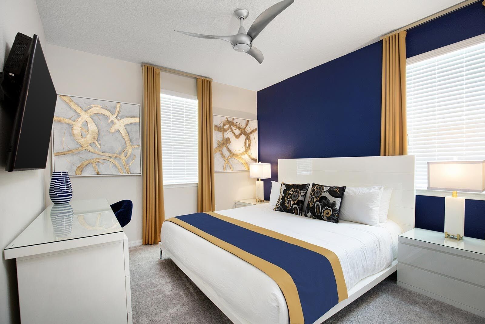 A hotel room with a bed, a desk, a TV, and artwork on the walls.