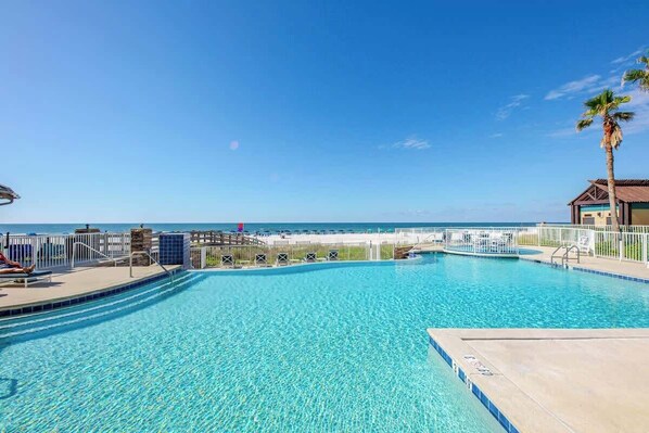 A clear blue pool with a view of the beach and ocean, surrounded by a white fence and a palm tree. - Upscale, beachfront *resort style pool *sleeps 10! (Orange Beach)