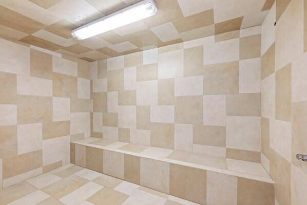 A bathroom with tiled walls and floor, a bench, and a ceiling light fixture.