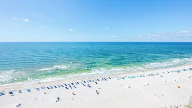 Een strand met rijen parasols en stoelen, een heldere lucht en de oceaan.
