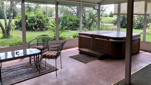 A covered patio area with a table and chairs, a hot tub, and a view of a lush garden. - Palm Coast Fairway Vista (Palm Coast)
