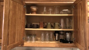 A wooden kitchen cabinet with multiple shelves containing various glassware, mugs, and jars. - Palm Coast Fairway Vista (Palm Coast)