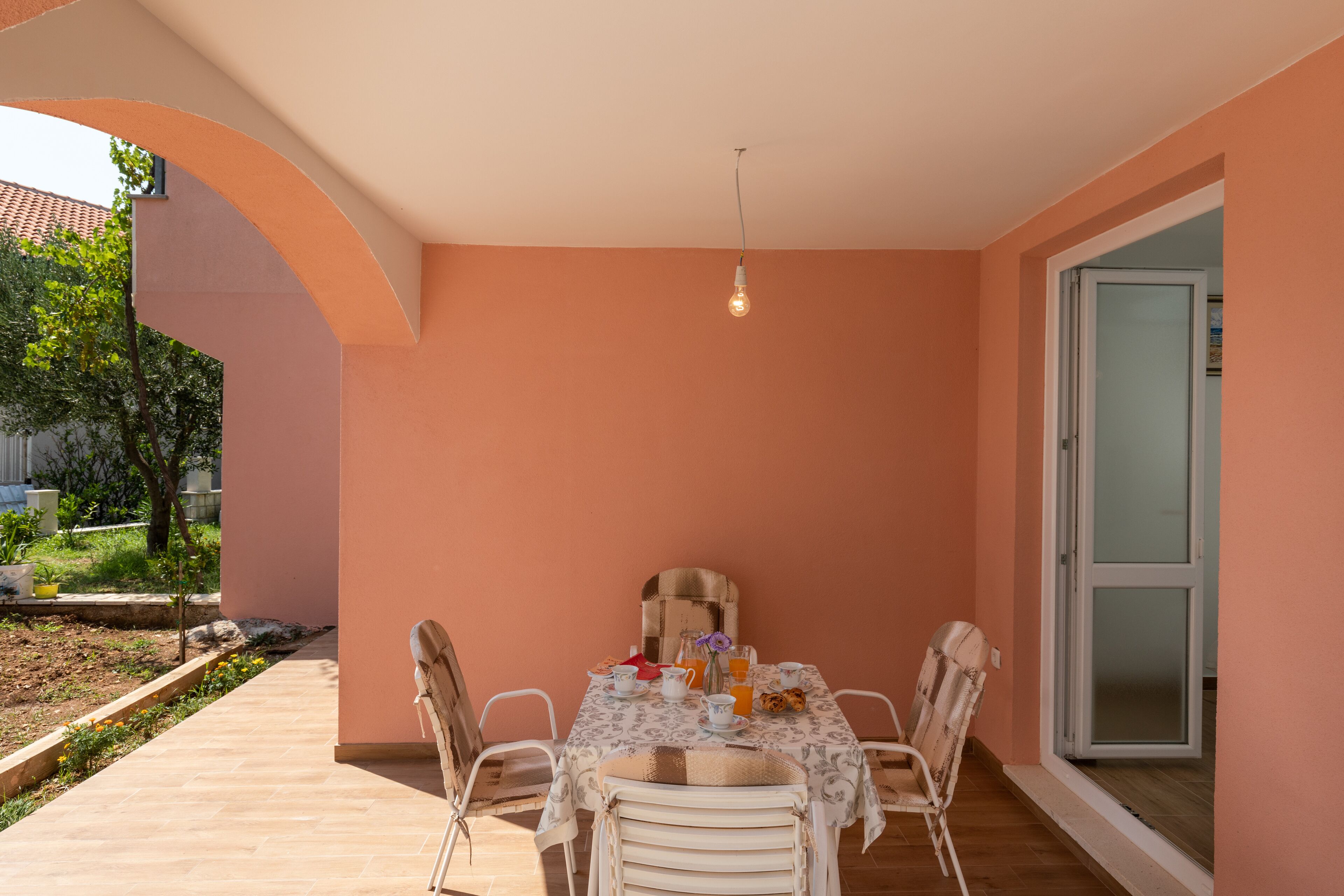 Uma área de refeições ao ar livre com uma mesa posta para dois, rodeada por cadeiras e um candeeiro pendente.