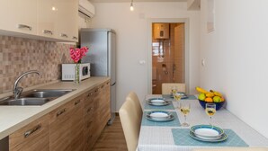 Una cocina moderna con microondas, lavamanos y armarios de madera. Hay una mesa de comedor dispuesta con platos, vasos y un cuenco de fruta.