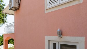 Un edificio con fachada rosa, una puerta blanca con panel de vidrio y una ventana con contraventanas blancas.
