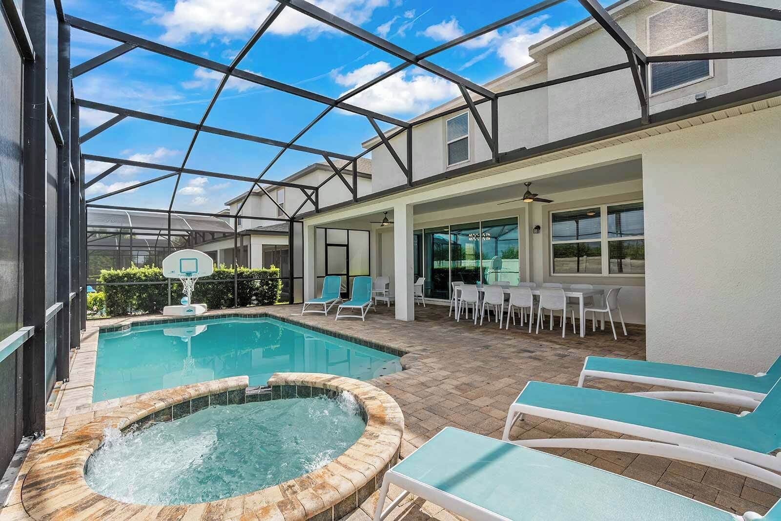 A covered outdoor swimming pool with lounge chairs and a hot tub, surrounded by a glass-enclosed patio area.